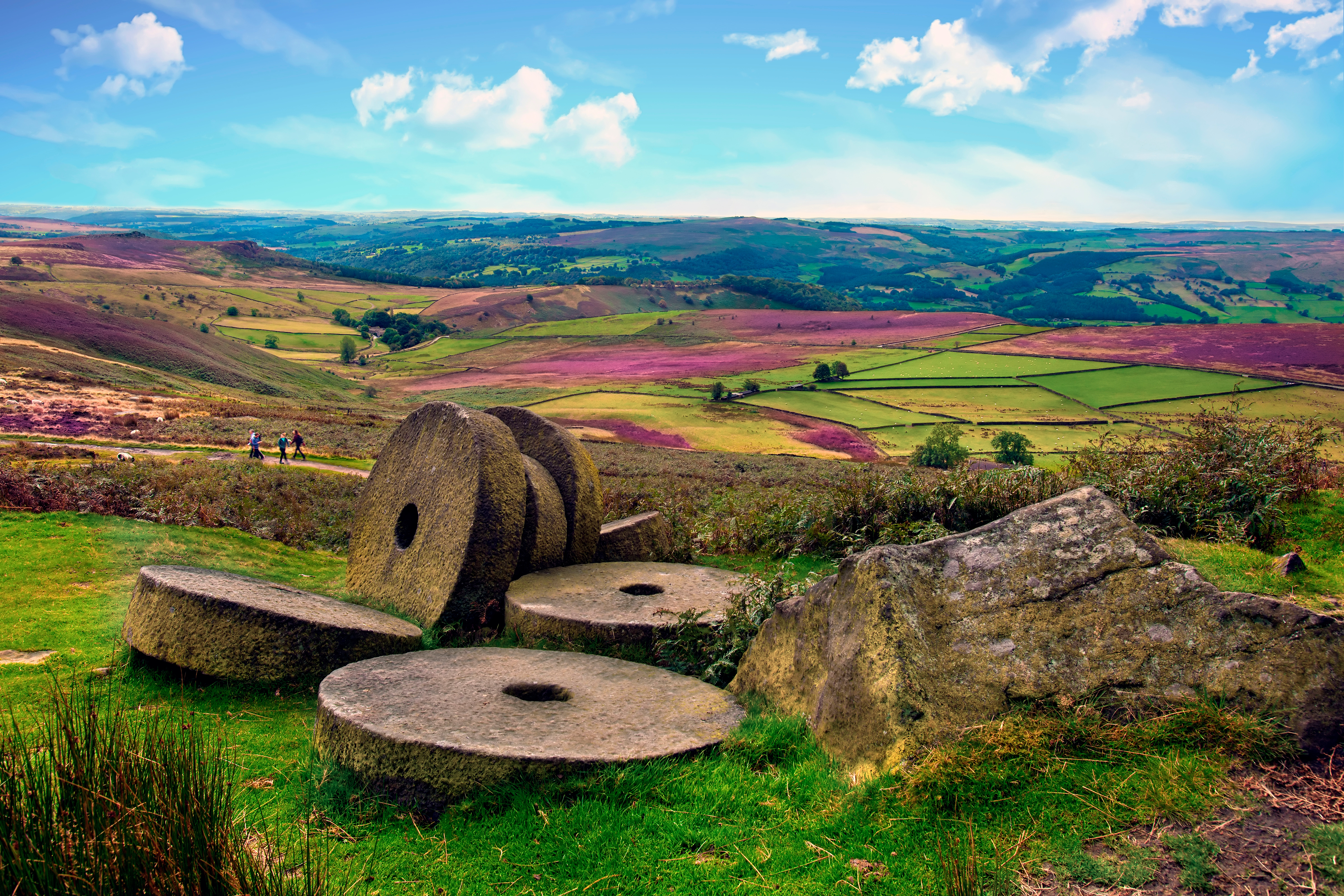 Weathered, abandoned millstones resting on the moors near Stanage Edge, surrounded by heather and rugged Peak District landscape